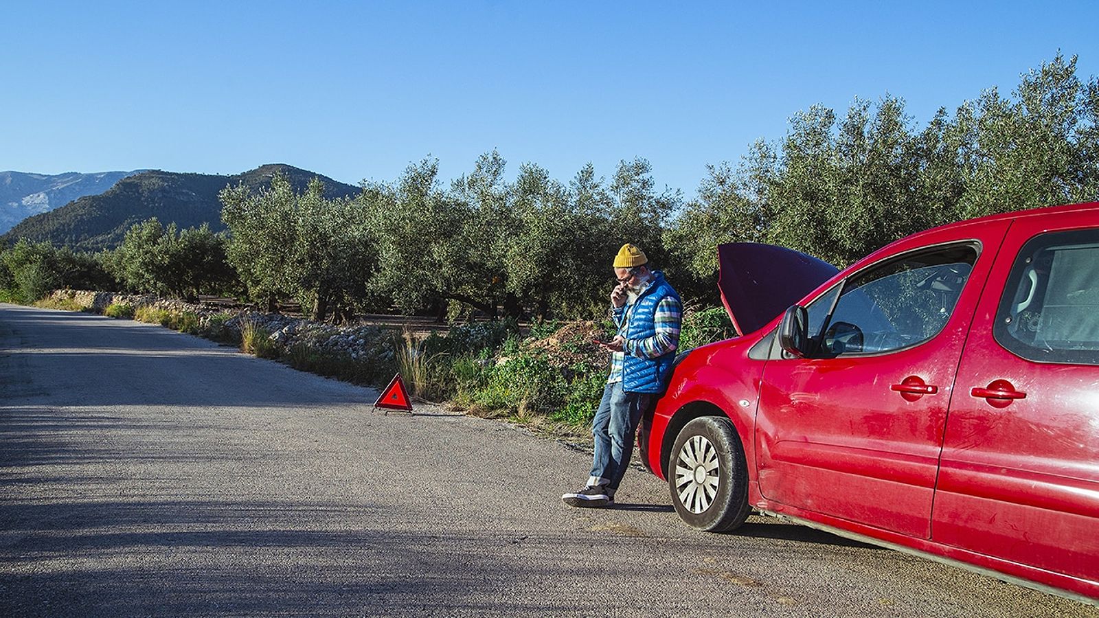 Man with relaxed attitude stranded on the road next to the broken down car talking on the phone